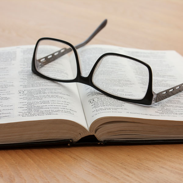 Open Bible with glasses sitting on top of it.